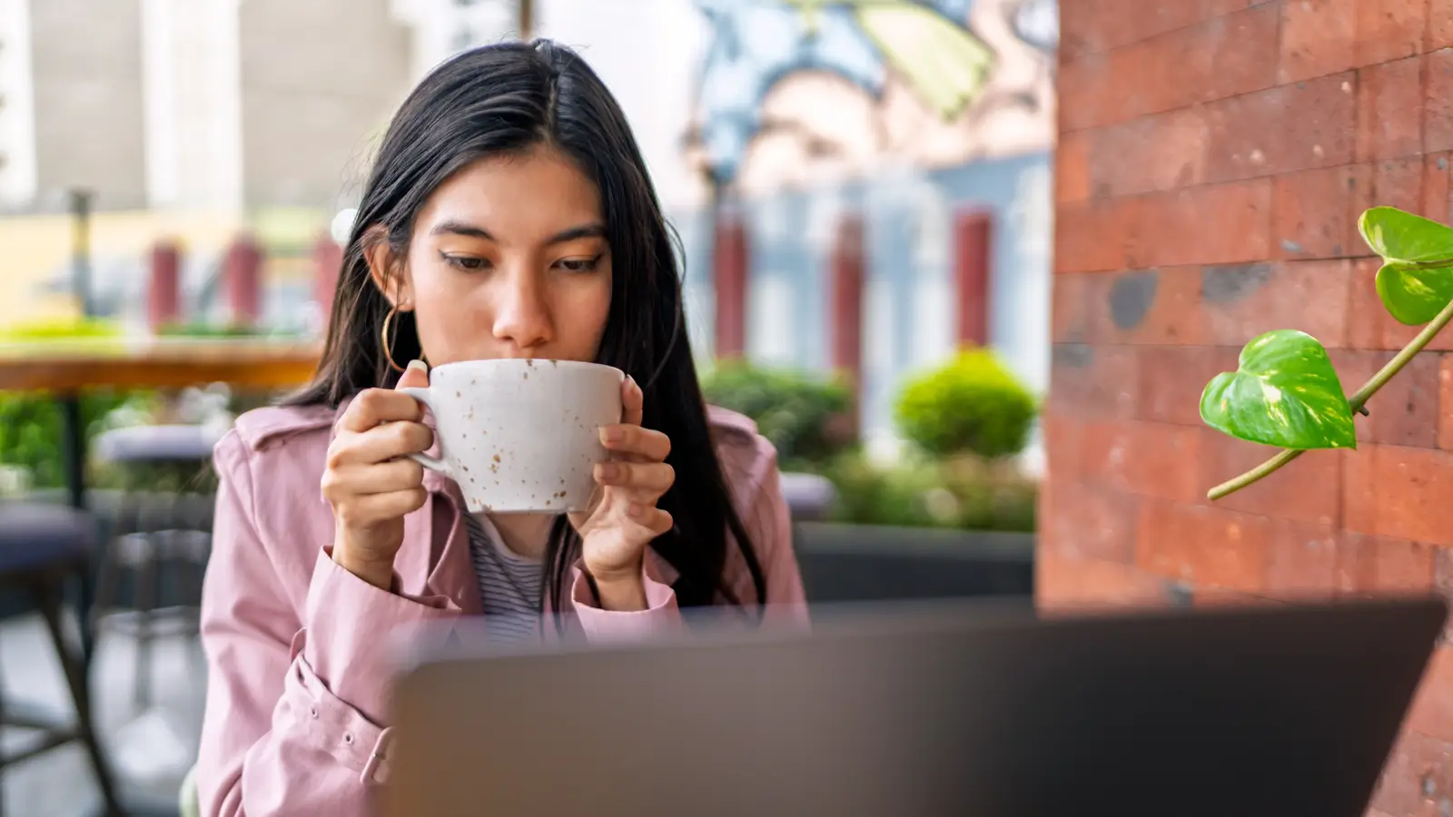 A woman sipping coffee in front of her laptop at a café table.